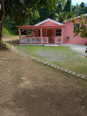 A pink building with a covered porch, a gated entrance, and a paved driveway.