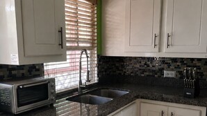 A kitchen with white cabinets, a built-in microwave, a sink, and a window with blinds.