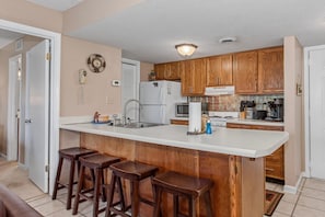 A kitchen with wooden cabinets, a white countertop, a refrigerator, a microwave, and a sink. There are three wooden stools at the counter. - Mountain View Memories Unit #2102 (Gatlinburg)