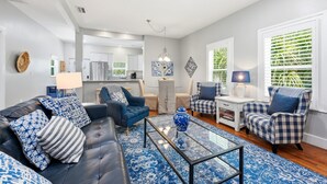 Uma sala de estar moderna com um sofá de couro preto, almofadas estampadas em azul, uma mesa de centro de vidro e um tapete com padrão azul.