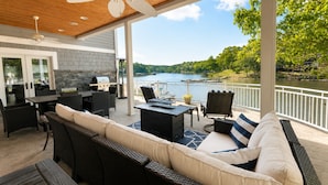 Un patio exterior techado con zona de comedor, asientos y vista al lago.