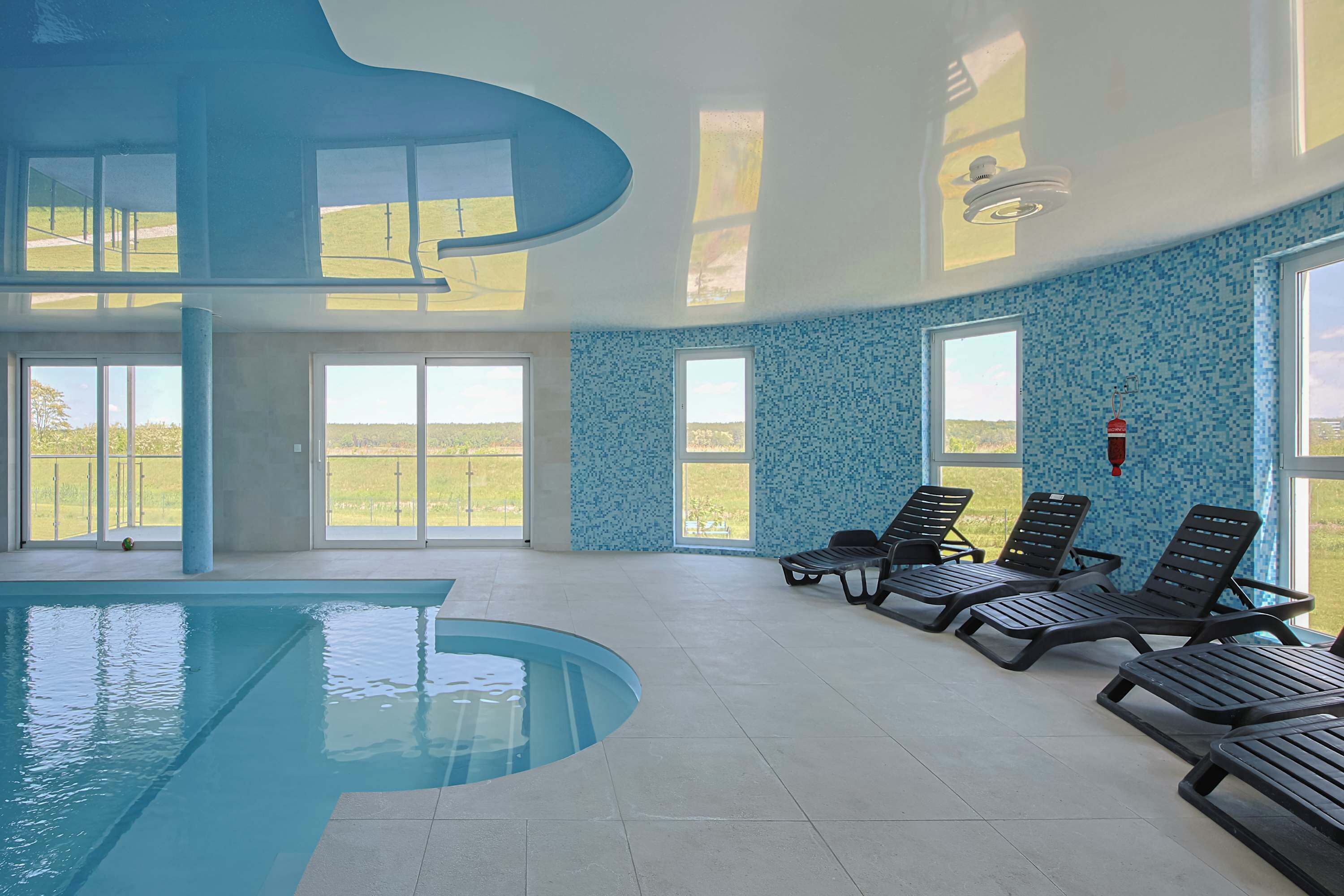 Una piscina interior amb parets de vidre transparent, gandules i vistes a l'exterior.