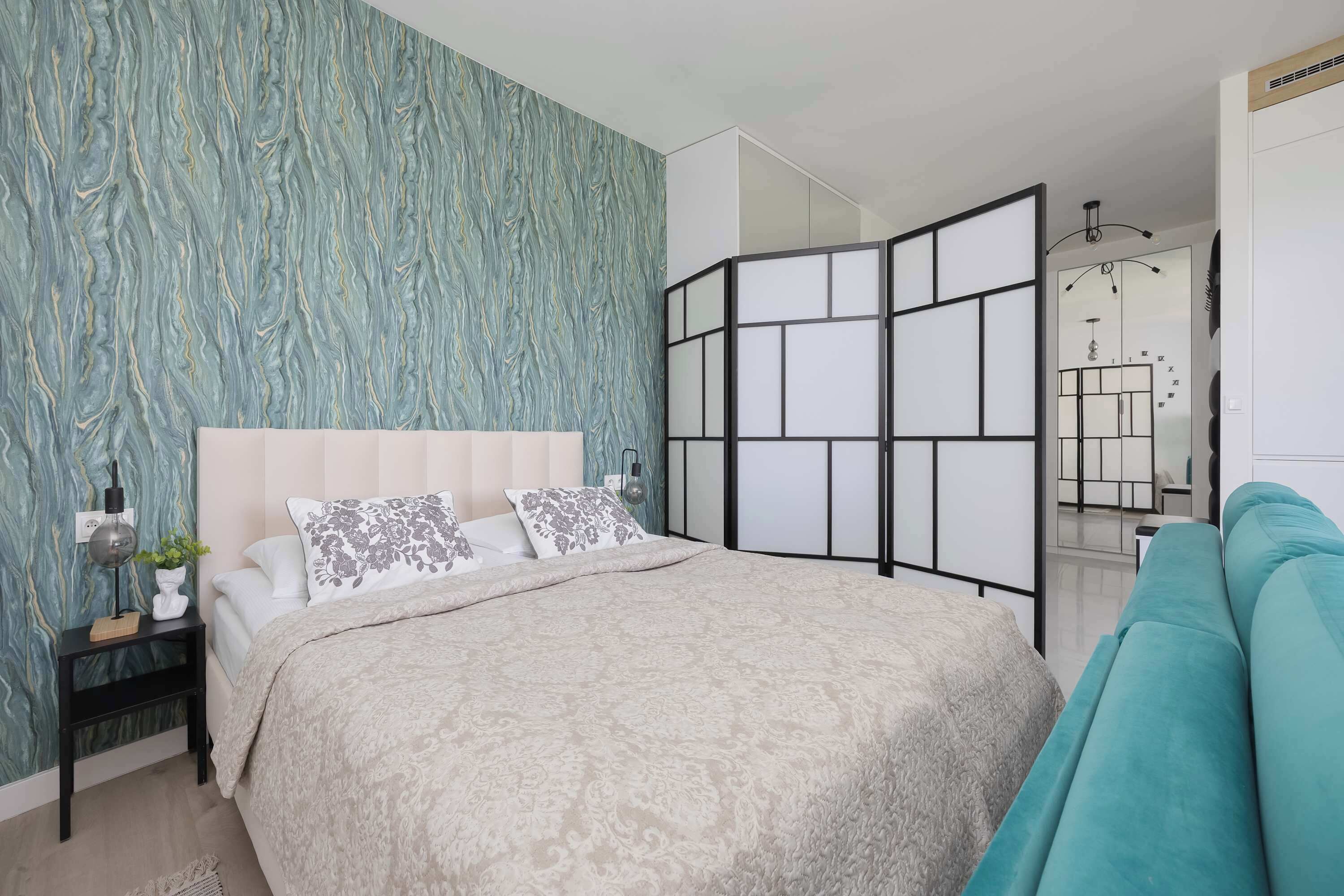 A bedroom with a bed, nightstand, and a decorative wall.