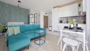 Een moderne woonkamer met een blauwgroene bank, een glazen salontafel, en een eethoek met een witte tafel en stoelen.