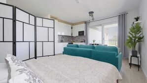 Een moderne slaapkamer met een groot bed, een bank, een kitchenette en een balkon met een plant.