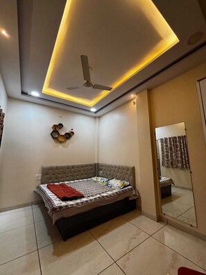 Une chambre à coucher comprenant un lit, un ventilateur de plafond, un éclairage encastré et un miroir.