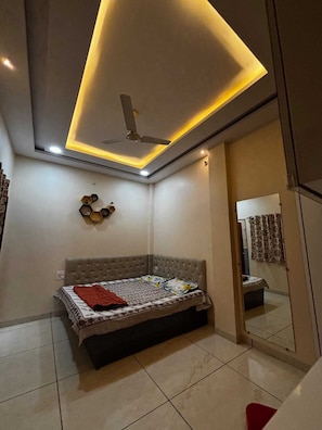 Un dormitorio con cama, ventilador de techo, iluminación empotrada y un espejo.