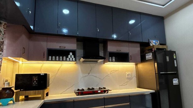 A modern kitchen with dark cabinets, a built-in stove, and a black refrigerator. - Vardaan Homestay  (Ujjain)