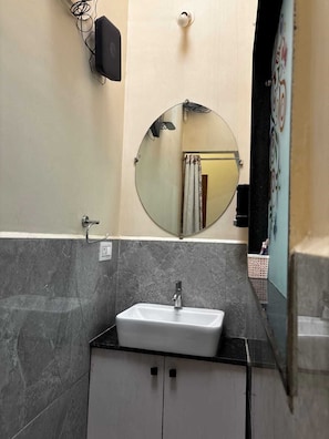 Un baño con un lavabo blanco, un espejo redondo y una encimera negra.