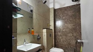 A bathroom with a sink, toilet, shower, and a red bucket. - Vardaan Homestay  (Ujjain)