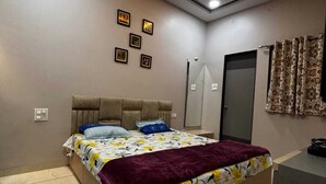 A bedroom with a bed, ceiling fan, recessed lighting, and a door. - Vardaan Homestay  (Ujjain)