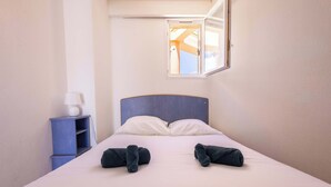 Une chambre d’hôtel avec un lit, deux serviettes enroulées, une table de chevet, une lampe et une fenêtre donnant sur un paysage.