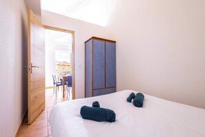 Een slaapkamer met een bed, twee handdoeken, een kledingkast en een deur naar een eetgedeelte.