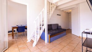 Une pièce avec un escalier, un canapé-lit, une table à manger avec des chaises et un meuble pour la télévision.
