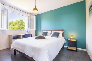 Une chambre à coucher comprenant un lit, un bureau, une table de chevet et une fenêtre donnant sur un paysage verdoyant.