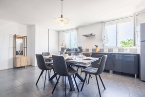 A modern kitchen with a dining area, featuring a large table, chairs, and a pendant light. - Air-conditioned apartment with outdoor space — Domaine Les Castans, between Agde and Pézenas (Saint-Thibéry)