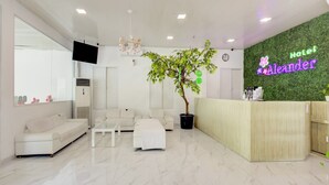 Ein Hotel-Empfangsbereich mit einer Rezeption, einem Blumentopf, einer Uhr und einer Sitzecke mit einer Couch und Sesseln.