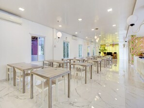 A spacious dining area with marble flooring, multiple tables, and chairs, and a brick accent wall with greenery. - Luxury Twin Stay With Free Wifi and Parking (Jakarta)