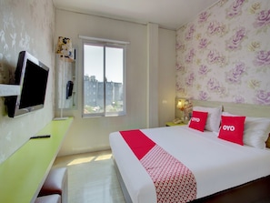 A hotel room with a bed, a desk, a TV, a window with a view, and floral wallpaper. - Luxury Twin Stay With Free Wifi and Parking (Jakarta)