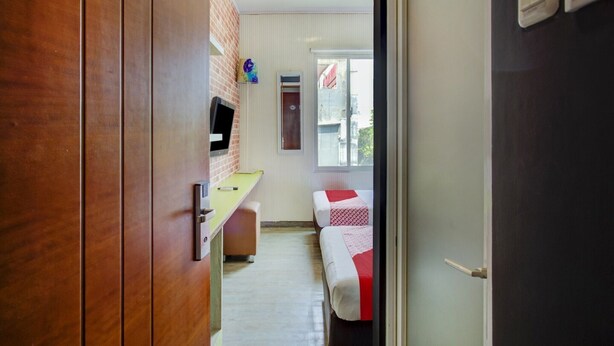Ein Flur, der zu einem Zimmer mit einem Bett, einem Schreibtisch, einem Fernseher und einem Fenster mit Blick auf Gebäude führt.