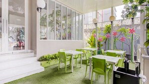 Ein Café mit grünen Stühlen und weißen Tischen, großen Fenstern und einem grünen Teppich.