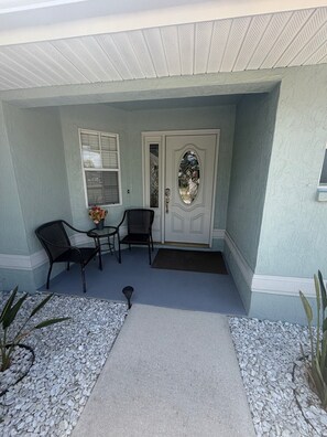 A house entrance with a covered porch, two chairs, a small table, and a decorative door.