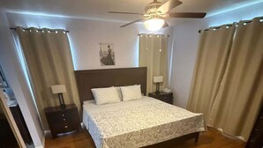 Een slaapkamer met een bed, een plafondventilator, twee nachtkastjes en een bedbank.