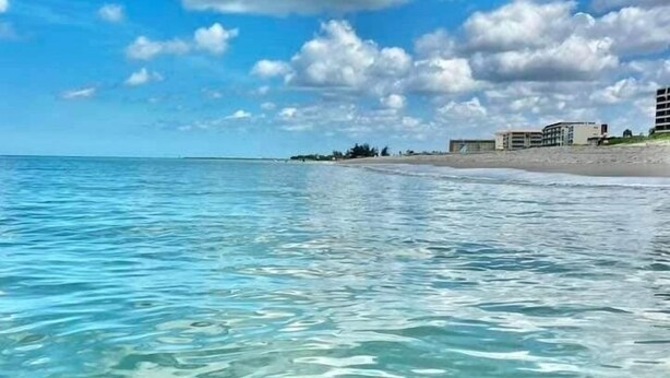 Een heldere blauwe zee met een zandstrand en gebouwen op de achtergrond.