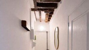 Un couloir étroit au plancher en bois, une porte blanche sur la droite et un plafond avec des poutres apparentes.