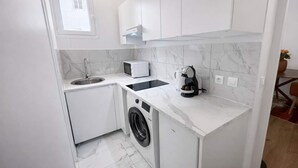 Une cuisine compacte équipée d’un lave-linge, d’un four à micro-ondes et d’une machine à café.