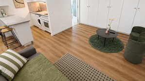 A modern kitchen with a sink, stove, and washing machine, a dining area with a round table and chairs, and a living space with a sofa and a green rug. - Charmant Studio Paris 11 - faubourg du temple (Paris)