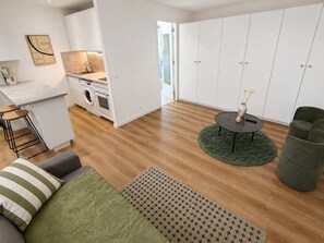A modern kitchen with a sink, stove, and washing machine, a dining area with a round table and chairs, and a living space with a sofa and a green rug. - Charmant Studio Paris 11 - faubourg du temple (Paris)