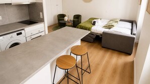 A compact living space with a kitchenette, a bed, a round mirror, and two stools. - Charmant Studio Paris 11 - faubourg du temple (Paris)