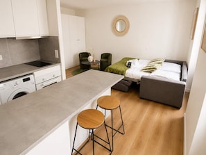 A compact living space with a kitchenette, a bed, a round mirror, and two stools. - Charmant Studio Paris 11 - faubourg du temple (Paris)