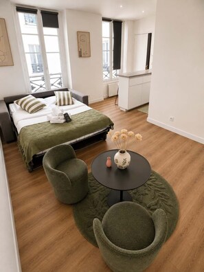 Una habitación de hotel moderna con cama, zona de estar con una mesa redonda y una kitchenette al fondo.