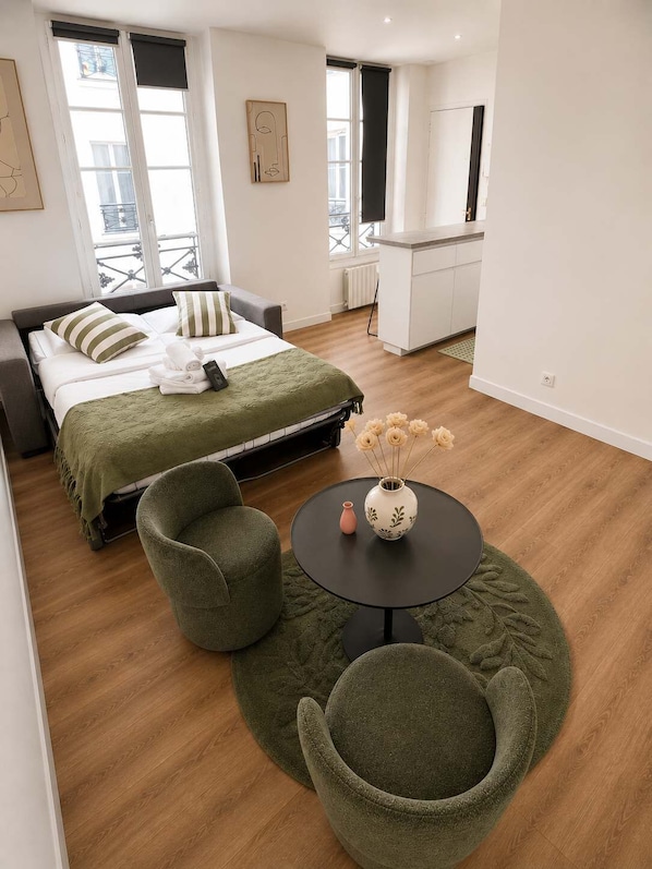A modern hotel room with a bed, a sitting area with a round table, and a kitchenette in the background. - Charmant Studio Paris 11 - faubourg du temple (Paris)