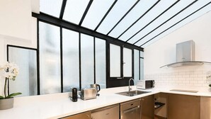 A modern kitchen with a large window, stainless steel appliances, and a white countertop. - Duplex Design Montparnasse - Baby-foot - 6P (Paris)