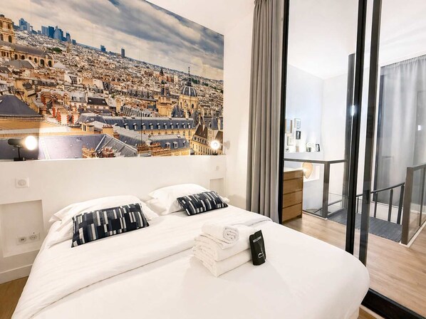 Ein Hotelzimmer mit Bett, einem Stadtbildgemälde, einem Balkon mit Blick und einem Willkommensschild.