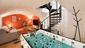 A room with a foosball table, a sofa, a lamp, and a staircase. - Duplex Design Montparnasse - Baby-foot - 6P (Paris)
