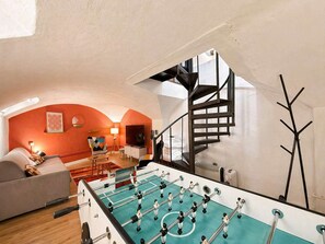 Ein Zimmer mit Kicker, einer Couch, einer Lampe und einer Treppe.