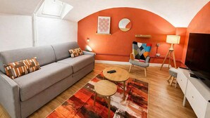 A living room with a sofa, two round tables, a television, and a wall-mounted lamp. - Duplex Design Montparnasse - Baby-foot - 6P (Paris)