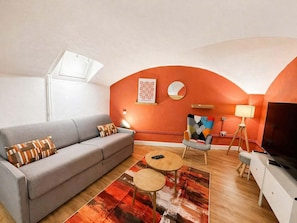 Ein Wohnzimmer mit einer Couch, zwei runden Tischen, einem Fernseher und einer Wandlampe.