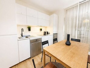 A modern kitchen with white cabinets, a wooden dining table, and a black vase. - Appartement Élégant -  Montparnasse - 6 Personnes (Paris)