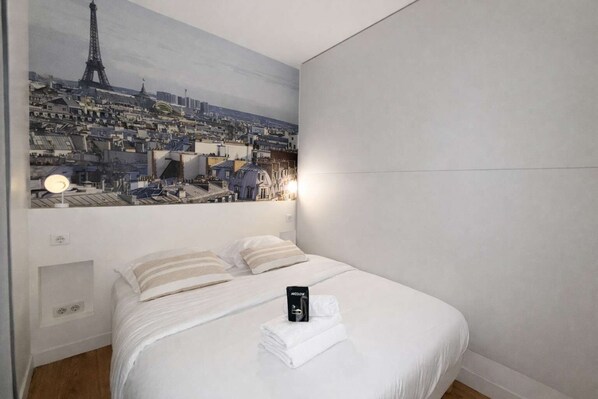 A hotel room with a bed, a painting of a cityscape, and a nightstand with a lamp.