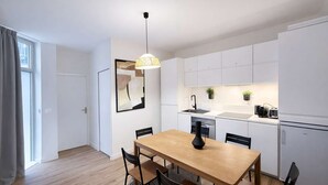 A modern kitchen with white cabinets, a dining table with chairs, a pendant light, and a black vase. - Appartement Élégant -  Montparnasse - 6 Personnes (Paris)
