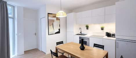 Una cocina moderna con armarios blancos, una mesa de comedor con sillas, una lámpara colgante y un florero negro.