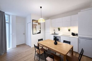 A modern kitchen with white cabinets, a dining table with chairs, a pendant light, and a black vase.