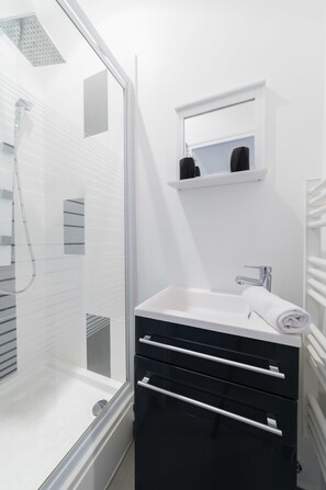 Een moderne badkamer met een glazen douchecabine, een witte wastafel met een handdoek en een spiegel erboven.