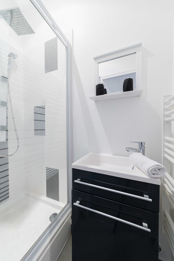 Une salle de bain moderne avec une douche à parois de verre, un lavabo blanc avec une serviette et un miroir au-dessus du lavabo.