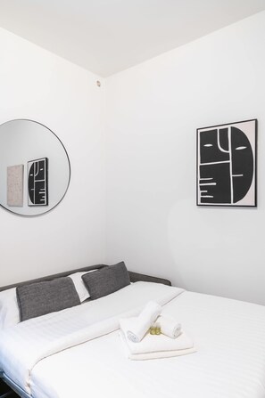 Een hotelkamer met een bed, een ronde spiegel en twee ingelijste kunstwerken aan de muur.